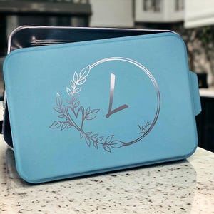 May include: A light blue baking pan with a silver design of a clock with a heart and leaves. The clock face says "Love".