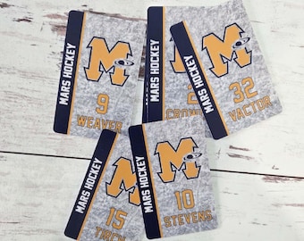 May include: A collection of hockey-themed cards with the text "MARS HOCKEY" in navy blue. Each card features a large gold "M" logo and player numbers with names. The cards have a textured gray background.