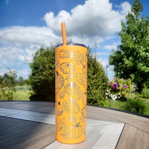 May include: Orange stainless steel tumbler with a black and white design of pumpkins and leaves. The tumbler has a straw.