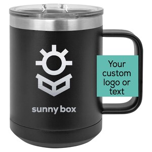 May include: Black stainless steel travel mug with a silver lid and a black handle. The mug has a white logo with a sun and a box, and the text "sunny box". The mug has a space for a custom logo or text.