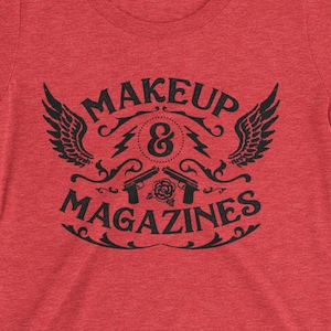 Puede incluir: Camiseta roja para mujer con un dise&ntilde;o gr&aacute;fico negro que dice "Makeup & Magazines" con un dise&ntilde;o alado estilizado y dos pistolas.