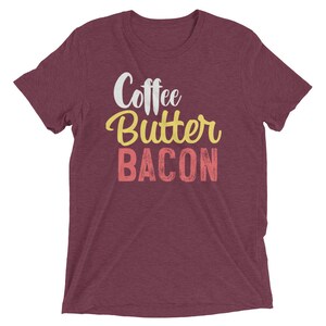 May include: Burgundy heather t-shirt with the text "Coffee Butter Bacon" in white, yellow, and pink.