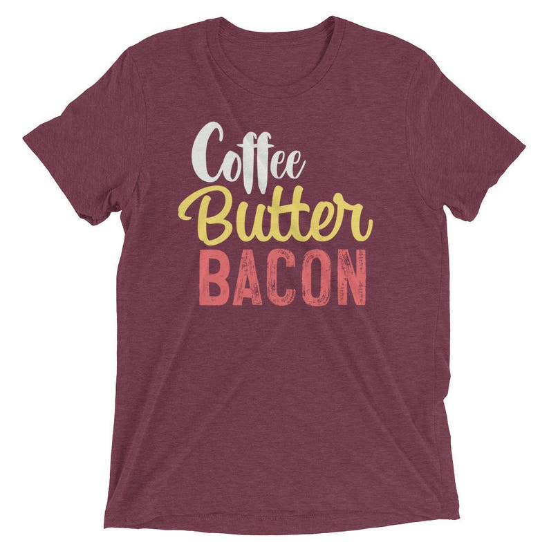 May include: Burgundy heather t-shirt with the text "Coffee Butter Bacon" in white, yellow, and pink.