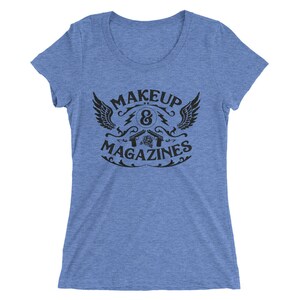 Puede incluir: Una camiseta azul claro con un dise&ntilde;o gr&aacute;fico negro que presenta un s&iacute;mbolo alado, el texto "MAKEUP & MAGAZINES" y dos pistolas cruzadas con una rosa en el centro.