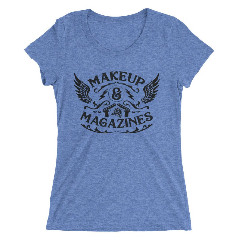 Puede incluir: Una camiseta azul claro con un dise&ntilde;o gr&aacute;fico negro que presenta un s&iacute;mbolo alado, el texto "MAKEUP & MAGAZINES" y dos pistolas cruzadas con una rosa en el centro.