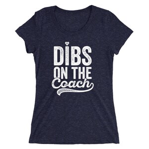 Puede incluir: Camiseta azul marino con la frase "Dibs on the Coach" en blanco, con un peque&ntilde;o coraz&oacute;n sobre la "i" de "Dibs". El texto est&aacute; en negrita, ligeramente desgastado, con un adorno decorativo debajo de la palabra "Coach".