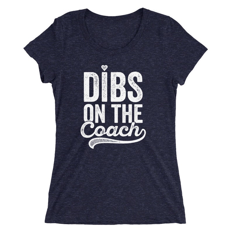 Puede incluir: Camiseta azul marino con la frase "Dibs on the Coach" en blanco, con un peque&ntilde;o coraz&oacute;n sobre la "i" de "Dibs". El texto est&aacute; en negrita, ligeramente desgastado, con un adorno decorativo debajo de la palabra "Coach".