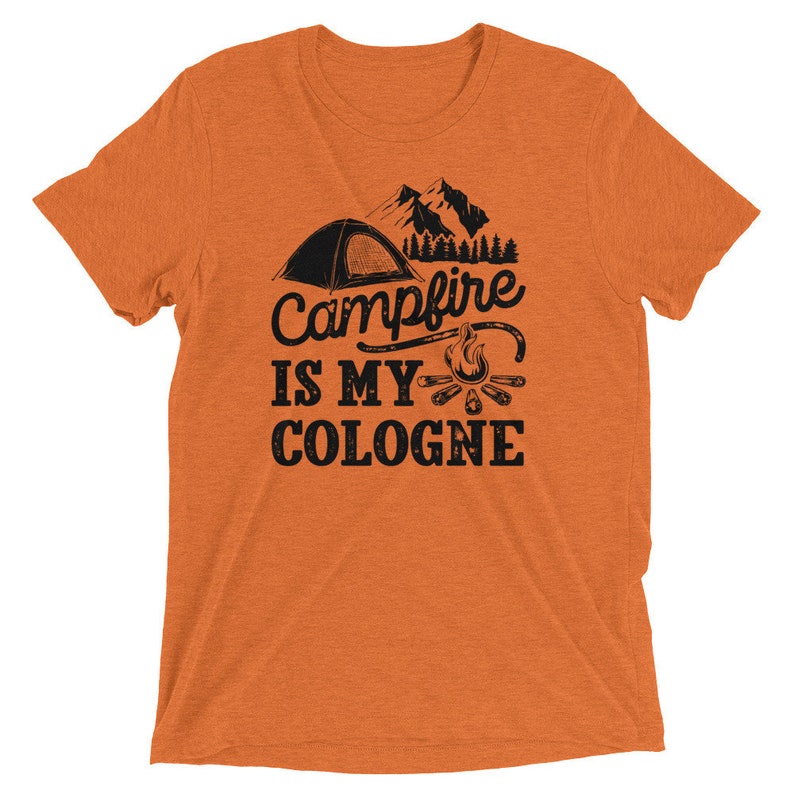 May include: Orange t-shirt with a black graphic of a tent, campfire, and mountains. The text reads "Campfire is my cologne".