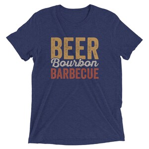 May include: A navy blue t-shirt with the text "BEER Bourbon BARBECUE" in a vintage style font. The text is in shades of yellow, orange, and red.