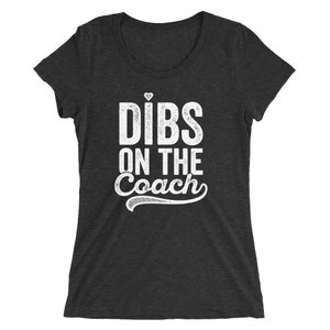 Puede incluir: Camiseta gris oscuro con el texto blanco "Dibs on the Coach", con un peque&ntilde;o coraz&oacute;n encima de "Dibs". El texto est&aacute; en negrita, ligeramente desgastado. La camiseta tiene cuello redondo y mangas cortas.