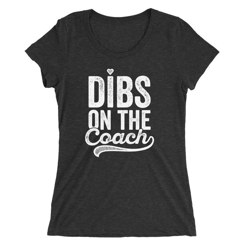 Puede incluir: Camiseta gris oscuro con el texto blanco "Dibs on the Coach", con un peque&ntilde;o coraz&oacute;n encima de "Dibs". El texto est&aacute; en negrita, ligeramente desgastado. La camiseta tiene cuello redondo y mangas cortas.