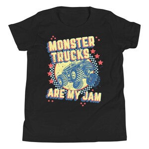 May include: Black youth t-shirt with a retro-style graphic of a monster truck. The graphic features a blue monster truck with yellow wheels and a red, white, and blue star pattern. The text "Monster Trucks Are My Jam" is printed in yellow, red, and blue.