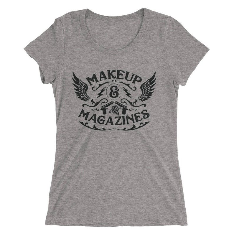 Puede incluir: Camiseta gris con un dise&ntilde;o gr&aacute;fico negro que dice "MAKEUP & MAGAZINES" con un dise&ntilde;o estilizado de alas, pistolas y una rosa.