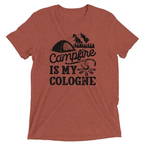 May include: A rust-colored t-shirt with a black graphic of a tent, mountains, a campfire, and the text "Campfire is my cologne".
