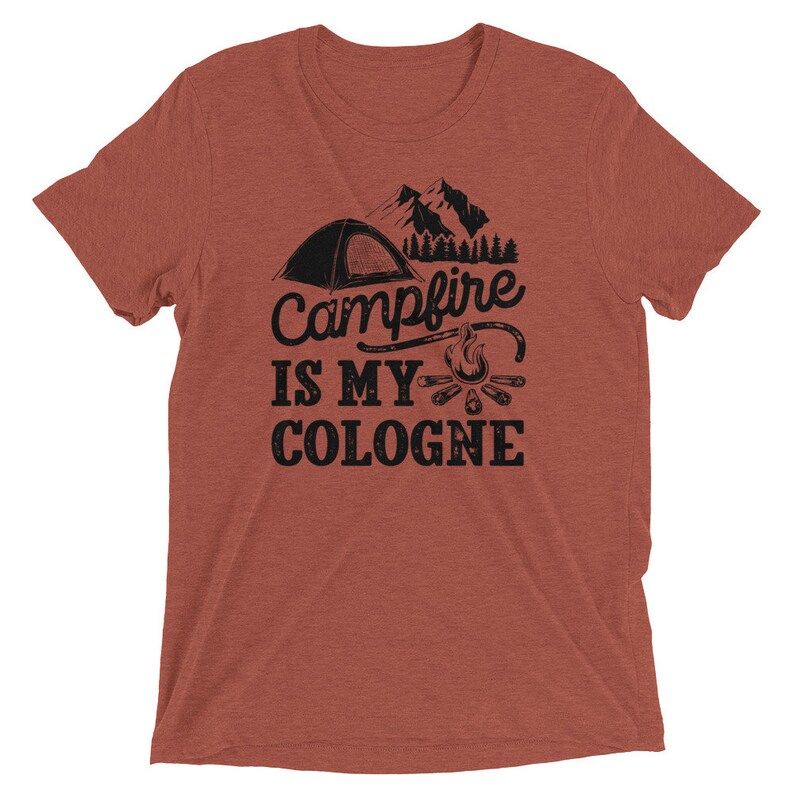 May include: A rust-colored t-shirt with a black graphic of a tent, mountains, a campfire, and the text "Campfire is my cologne".