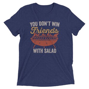 May include: A navy blue t-shirt with the text "You don't win friends with salad" in white. A red and orange grill with flames is above the text.