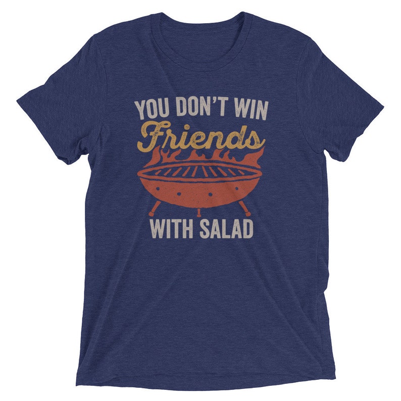 May include: A navy blue t-shirt with the text "You don't win friends with salad" in white. A red and orange grill with flames is above the text.