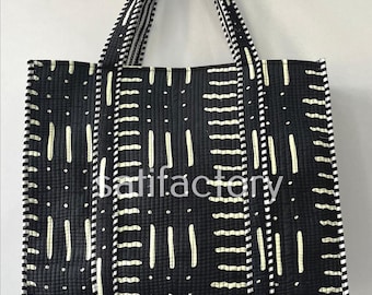 Può includere: Borsa tote nera con un motivo geometrico di linee verticali e punti bianchi. La borsa ha manici a righe bianche e nere abbinati e la parola "satisfactory" stampata sul davanti.