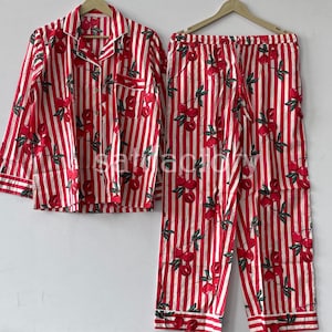 May include: Red and white striped pajama set with a cherry pattern. The long-sleeved button-down shirt and pants feature a repeating design of red cherries with green leaves. The set is displayed on a hanger.