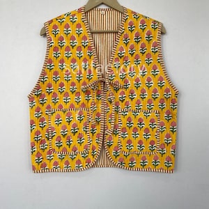 May include: A yellow quilted vest with a floral pattern in pink and green. The vest has a striped lining and two front pockets. It is sleeveless and ties in the front.