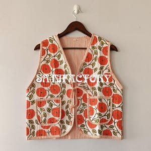 May include: A quilted vest with a floral pattern of orange flowers and green leaves on a white background. The vest has two pockets and a tie closure. The text "SATISFACTORY" is printed on the vest.