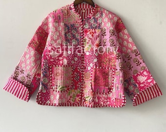 Op de afbeelding: Een roze gewatteerde jas met een patchwork ontwerp met bloemen- en geometrische patronen. De jas heeft een opstaande kraag, twee voorzakken en gestreepte manchetten. De jas hangt aan een houten hanger.