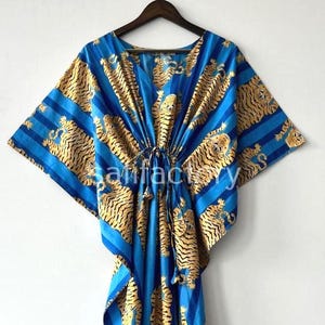 May include: Blue and gold tiger print caftan. The caftan features a V-neck and a drawstring waist. The fabric has a striped pattern with gold tiger illustrations. The caftan is a loose-fitting garment.