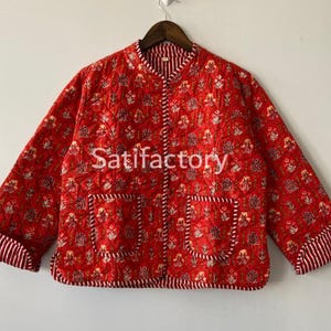 May include: Red quilted jacket with a floral pattern and two front pockets. The jacket has a mandarin collar and striped cuffs. The text "Satifactory" is printed on the front.