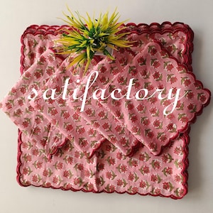 Pode incluir: Conjuntos de individuais e guardanapos com estampas florais rosa, bordas onduladas e acabamento em vermelho escuro. O texto "satisfactory" é impresso na imagem. Uma planta decorativa com folhas amarelas e verdes é colocada em cima.