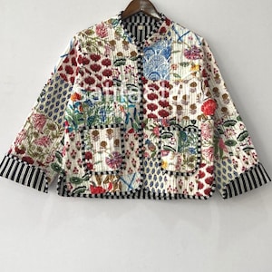 Puede incluir: Chaqueta acolchada con diseño patchwork con estampados florales y geométricos en rojo, azul, verde y blanco. La chaqueta tiene un ribete a rayas blancas y negras en los puños y el dobladillo.