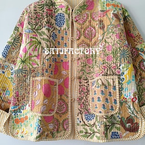 K&ouml;nnte beinhalten: Gesteppte Jacke mit Patchwork-Design mit Blumenmustern in Rosa, Blau und Gr&uuml;n auf beigem Hintergrund. Die Jacke hat zwei Taschen und einen Stehkragen. Der Text "SATIFACTORY" ist auf der Jacke zu sehen.
