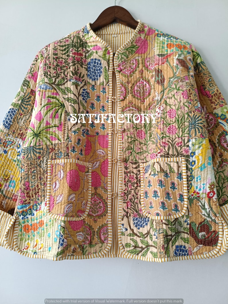 K&ouml;nnte beinhalten: Gesteppte Jacke mit Patchwork-Design mit Blumenmustern in Rosa, Blau und Gr&uuml;n auf beigem Hintergrund. Die Jacke hat zwei Taschen und einen Stehkragen. Der Text "SATIFACTORY" ist auf der Jacke zu sehen.