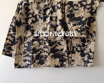 May include: A two-piece pajama set with a floral pattern. The set includes a button-down shirt and matching pants. The pajamas are black with a beige floral design and white trim. The text "SATIFACTORY" is visible on the shirt.