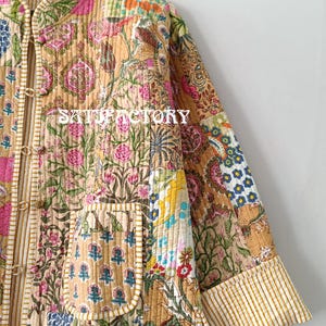 K&ouml;nnte beinhalten: Gesteppte Jacke mit Patchwork-Design. Sie hat verschiedene Blumen- und geometrische Muster in Beige, Rosa, Blau und Gr&uuml;n. Mit Stehkragen, zwei Taschen und Knopfleiste. Der Text "SATISFACTORY" ist sichtbar.