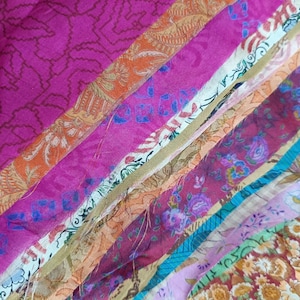 Può includere: Una collezione di ritagli di tessuto colorati in varie tonalità di rosa, arancione, blu e oro. I tessuti presentano disegni floreali e fantasia, creando un'esposizione vibrante e strutturata. Ideale per progetti di artigianato.