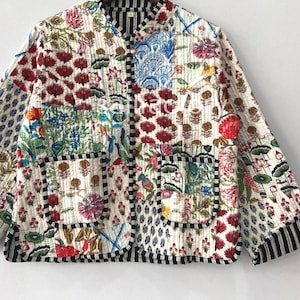 K&ouml;nnte beinhalten: Gesteppte Jacke mit Patchwork-Design mit Blumen- und Paisley-Mustern in Rot, Blau, Gr&uuml;n und Rosa auf wei&szlig;em Hintergrund. Die Jacke hat einen Stehkragen, schwarz-wei&szlig; gestreifte Paspeln und zwei Vordertaschen.