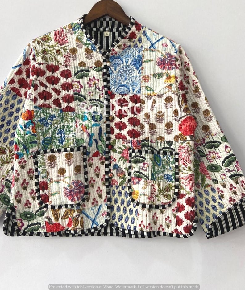 K&ouml;nnte beinhalten: Gesteppte Jacke mit Patchwork-Design mit Blumen- und Paisley-Mustern in Rot, Blau, Gr&uuml;n und Rosa auf wei&szlig;em Hintergrund. Die Jacke hat einen Stehkragen, schwarz-wei&szlig; gestreifte Paspeln und zwei Vordertaschen.