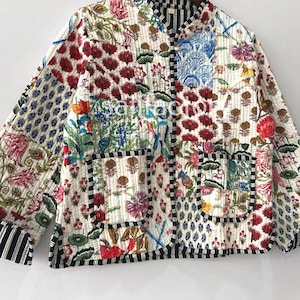 K&ouml;nnte beinhalten: Gesteppte Jacke mit Patchwork-Design mit Blumen- und geometrischen Mustern in Rot, Blau, Gr&uuml;n und Gelb auf cremefarbenem Hintergrund. Die Jacke hat einen schwarz-wei&szlig; gestreiften Besatz und zwei Taschen.