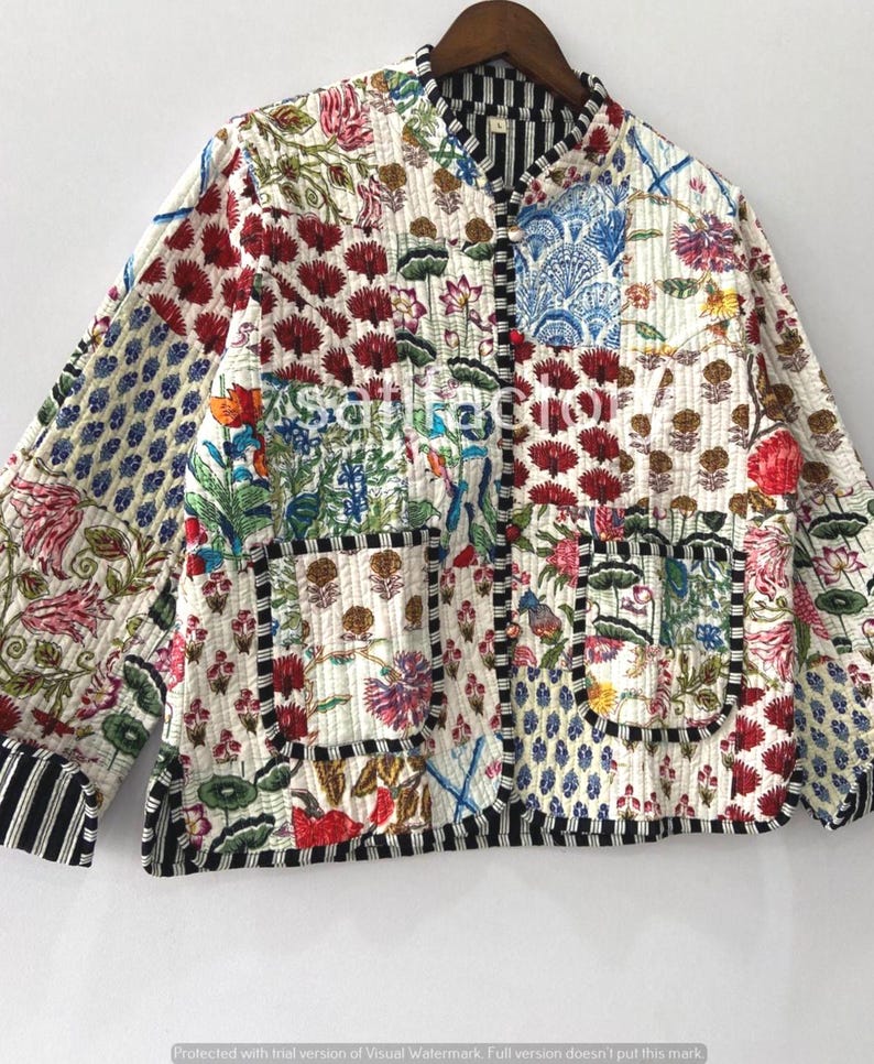 K&ouml;nnte beinhalten: Gesteppte Jacke mit Patchwork-Design mit Blumen- und geometrischen Mustern in Rot, Blau, Gr&uuml;n und Gelb auf cremefarbenem Hintergrund. Die Jacke hat einen schwarz-wei&szlig; gestreiften Besatz und zwei Taschen.
