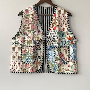 May include: A quilted vest with a floral pattern in shades of pink, green, blue, and orange on a cream background. The vest has black and white striped lining and black trim. Two pockets are visible on the front.