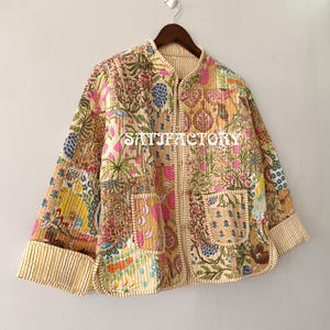 K&ouml;nnte beinhalten: Patchwork-Jacke mit floralem Muster in Rosa, Blau und Gelb. Die Jacke hat einen Stehkragen, zwei Taschen und gestreifte Manschetten. Der Text "SATISFACTORY" ist auf der Vorderseite aufgedruckt.