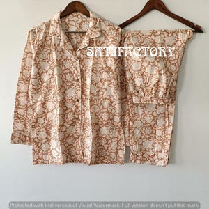 May include: A two-piece pajama set with a floral pattern in shades of brown and cream. The long-sleeved button-down shirt and pants are displayed on a wooden hanger. The text "SATISFACTORY" is visible on the image.
