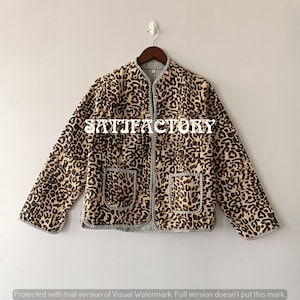 May include: A leopard print quilted jacket with two front pockets. The jacket is trimmed with a striped fabric and features the text "SATIFACTORY". The jacket is hanging on a wooden hanger.