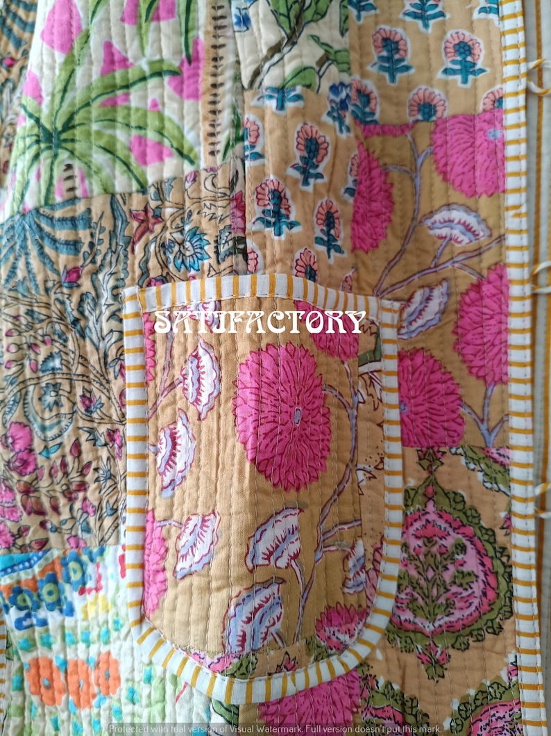 K&ouml;nnte beinhalten: Nahaufnahme eines Patchwork-Textils mit floralen und botanischen Mustern in Rosa-, Gr&uuml;n-, Blau- und Beiget&ouml;nen. Das Wort "SATISFACTORY" ist auf einer Tasche aufgedruckt. Das Textil ist mit wei&szlig;en N&auml;hten gesteppt.