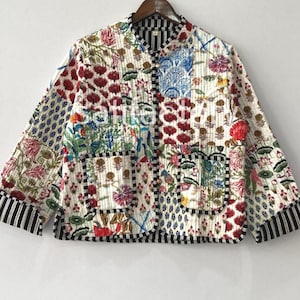 K&ouml;nnte beinhalten: Gesteppte Jacke mit Patchwork-Design mit floralen und geometrischen Mustern in Rot, Blau, Gr&uuml;n und Braun auf wei&szlig;em Hintergrund. Die Jacke hat einen Stehkragen, zwei Taschen und einen schwarz-wei&szlig; gestreiften Besatz an den Manschetten und am Saum.
