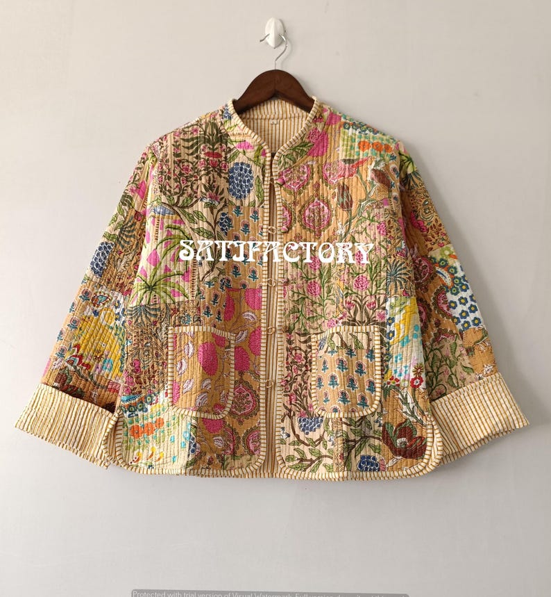 K&ouml;nnte beinhalten: Gesteppte Jacke mit Patchwork-Design mit floralen und botanischen Mustern in Rosa, Blau, Gelb und Gr&uuml;n. Die Jacke hat einen Stehkragen, zwei Vordertaschen und einen gestreiften Besatz. Das Wort "SATISFACTORY" ist auf der Vorderseite aufgedruckt.