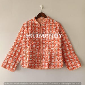 May include: An orange quilted jacket with a white floral pattern and two front pockets. The jacket is hanging on a wooden hanger against a neutral background. The text "SATIFACTORY" is visible on the jacket.