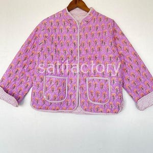 Könnte beinhalten: Gesteppte Jacke mit lavendelfarbenem Blumenmuster und zwei Vordertaschen. Die Jacke hat einen Stehkragen und ist wendbar mit einem Streifenmuster auf der Innenseite. Die Manschetten sind ebenfalls gestreift.