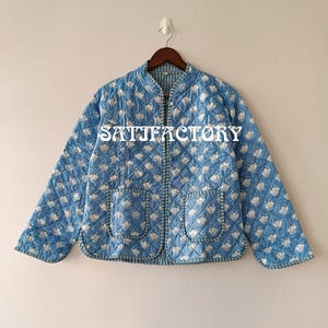 Könnte beinhalten: Blau gesteppte Jacke mit weißem Blumenmuster und zwei Vordertaschen. Die Jacke hat einen runden Kragen und einen Reißverschluss. Der Text "SATTIFACTORY" ist auf der Vorderseite aufgedruckt.
