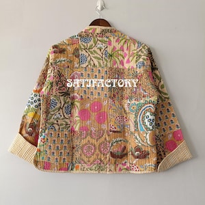 K&ouml;nnte beinhalten: Patchwork-Jacke mit verschiedenen Blumen- und Paisley-Mustern in Beige-, Rosa-, Blau- und Gr&uuml;nt&ouml;nen. Die Jacke hat einen Kragen und lange &Auml;rmel mit gestreiften Manschetten. Das Wort "SATIFACTORY" ist auf die Jacke gedruckt.